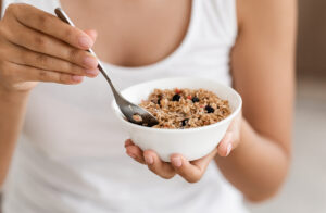 Closeup of bowl with fresh oatmeal and spoon in woman hands, healthy and nutritive breakfast concept. Unrecognizable lady holding delicious homemade granola, having breakfast at home