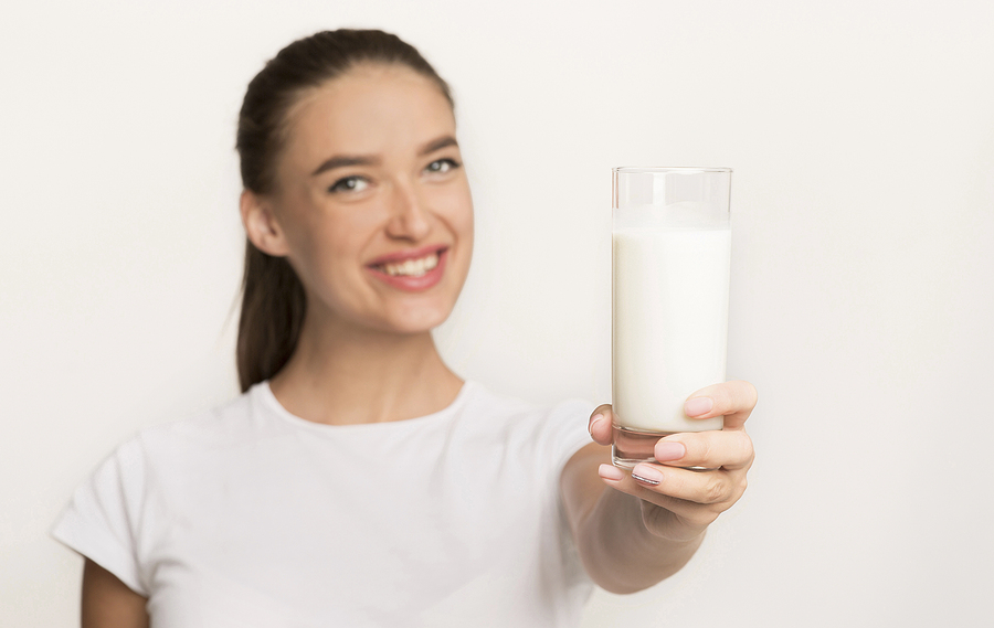 Dairy Products Benefits. Girl Offering Glass Of Milk To Camera Standing Over White Studio Background. Isolated, Shallow Depth